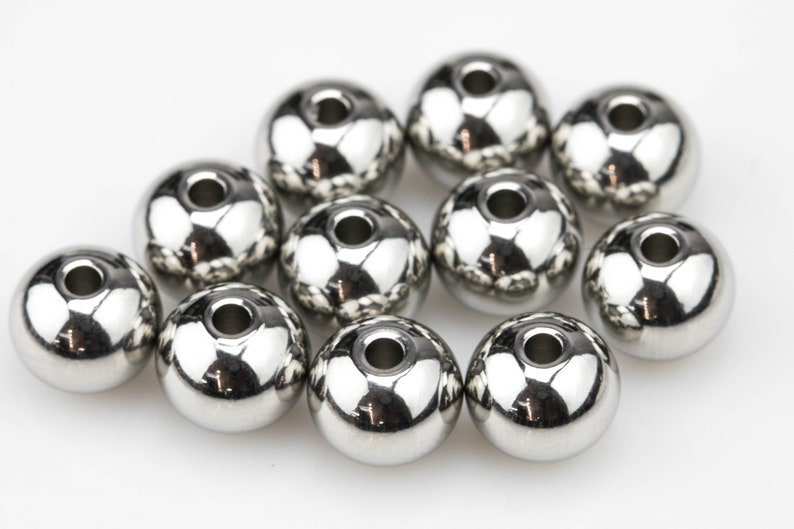 May include: A group of ten silver metal beads with a hole in the center of each bead.