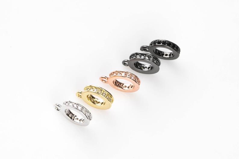 May include: Five different coloured metal rings with a row of clear crystals around the edge. The rings have a small loop at the top for attaching to a chain or other jewellery.