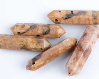 May include: Six polished, double-terminated gemstone pendants in shades of tan, brown, and cream. Each pendant has a hole drilled through one end. The gemstones are arranged on a white background.