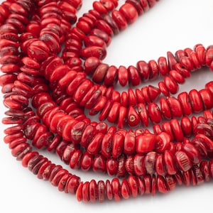 May include: A strand of red coral beads, each bead is a unique, irregular shape. The beads are strung together to create a long necklace.