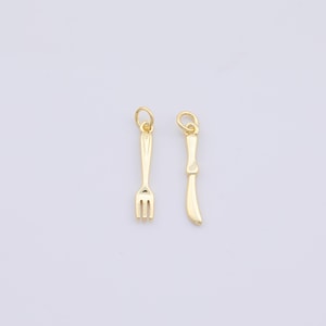 May include: Two gold-colored charms in the shape of miniature cutlery. One charm is a fork with three tines, and the other is a knife. Both charms have a small loop at the top for attaching to a chain or bracelet.