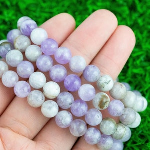 May include: A close-up of a hand holding a bracelet made of light purple and white beads. The bracelet is made of multiple strands of beads, and the beads are all round and smooth.