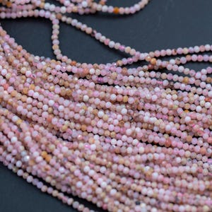 May include: Close-up of a collection of small, round, pink beads strung together. The beads have a slightly faceted appearance, catching the light. The color varies from pale pink to a deeper rose hue, with some beads showing hints of peach.