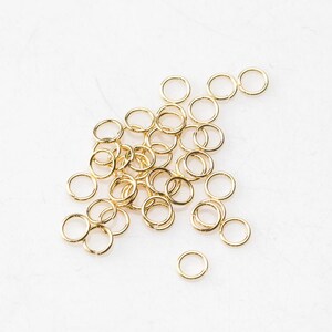 May include: A pile of gold jump rings, a type of jewellery finding used for connecting chains, cords, and other jewellery components.