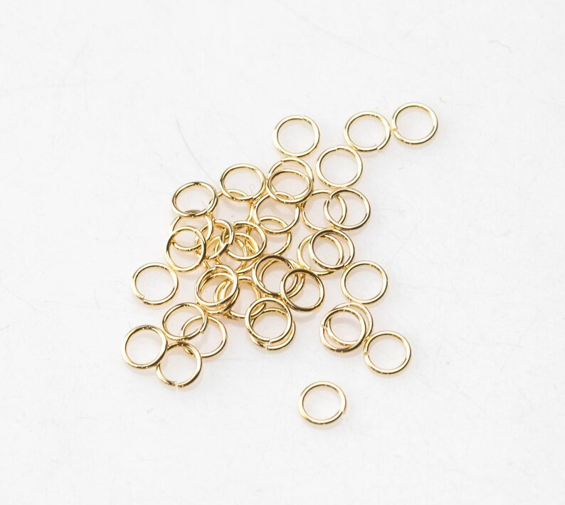 May include: A pile of gold jump rings, a type of jewellery finding used for connecting chains, cords, and other jewellery components.