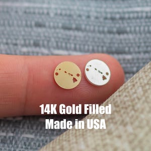 May include: Two small, round gold-filled pendants, one gold and one silver, each featuring a cutout of the Hawaiian Islands. The text "14K Gold Filled Made in USA" is displayed below the pendants.