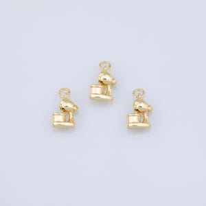 May include: Three gold-toned metal charms shaped like stand mixers. Each charm features a rounded top, a central arm, and a cylindrical base with a small circular jump ring attached to the top for hanging or connecting to jewellery pieces.