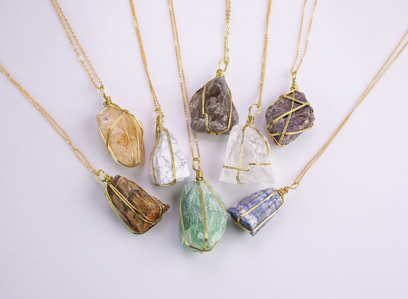 May include: A selection of gemstone necklaces. Each necklace has a raw, irregularly shaped stone wrapped in gold-coloured wire and suspended from a delicate gold chain. The stones vary in colour, including orange, white, brown, green, and purple.