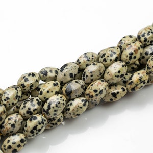 Könnte beinhalten: Eine Schnur ovaler Dalmatiner-Jaspisperlen. Die Perlen sind hellbeige mit schwarzen Flecken.