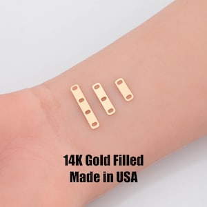 May include: Three gold-filled rectangular jewelry components with oval holes are displayed. The components are in varying sizes, with the largest having three holes and the smallest having one. The text "14K Gold Filled Made in USA" is at the bottom.