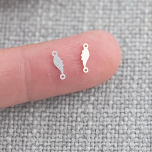 以下が含まれることがあります： 葉の形をした小さなループが付いた白い金属製のジュエリー金具が2つあります