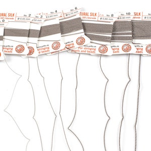 Pu&ograve; includere: Assortimento di dieci bobine di filo di seta naturale per infilare perline. Le bobine sono etichettate con i numeri da 0 a 16, e lo spessore del filo in millimetri. Il filo &egrave; di colore marrone chiaro.