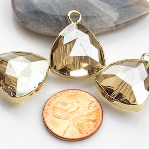 May include: Three gold-toned teardrop-shaped crystal pendants with a faceted design. The pendants are approximately the size of a UK penny.