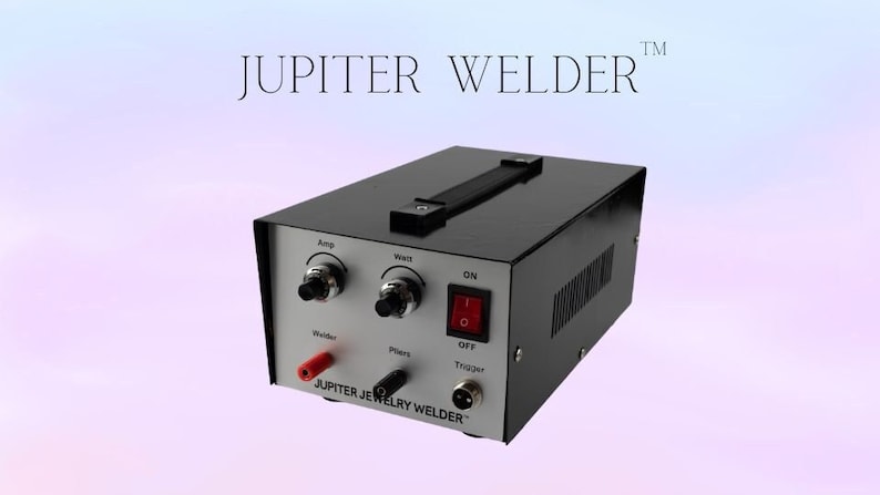 May include: A black and silver jewelry welder with a handle on top. The front panel has controls labeled "Amp", "Weld", "Pliers", and "Trigger". The power switch is labeled "ON" and "OFF". The text "JUPITER JEWELRY WELDER&trade;" is printed on the front panel.