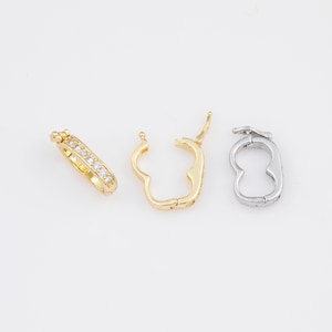 May include: Three earrings on a white background. One gold hoop earring with clear stones, and two open hoop earrings, one gold and one silver, each with a hinge closure. The earrings are designed for pierced ears.