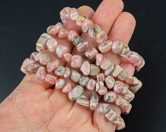 Puede incluir: Una hebra de cuentas de piedras preciosas rayadas de color rosa y blanco, pulidas y pulidas, en una mano.