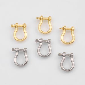 May include: Six metal shackle clasps in gold and silver tones. The clasps are U-shaped with a screw pin closure. The gold clasps have a shiny finish, while the silver clasps have a matte finish. These clasps are used for jewelry making.