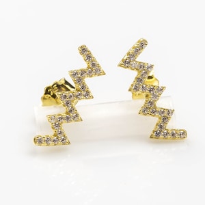 May include: A pair of gold earrings with a zig-zag design and clear cubic zirconia stones.