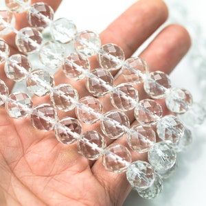 May include: A strand of clear faceted crystal beads, held in a hand. The beads are round and have a shiny, reflective surface.