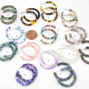 May include: Assortment of 14 pairs of colorful, patterned hoop earrings. The earrings are made of plastic and have a variety of designs, including tortoiseshell, marble, and floral patterns.