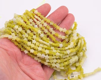 May include: Strands of star-shaped beads in shades of yellow and white are held in a hand. The beads are strung together, creating a textured and layered effect. The beads are likely for jewelry making or crafting.