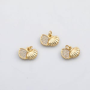 May include: Three gold-colored seashell charms with a loop for hanging. Each charm has a section of small, clear crystals. The seashell design is detailed with ridges and curves, creating a textured appearance. These charms are suitable for jewelry making.