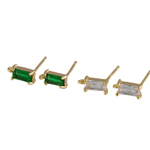 May include: A set of four gold stud earrings with rectangular shaped gemstones. Two earrings feature green gemstones and two earrings feature clear gemstones.