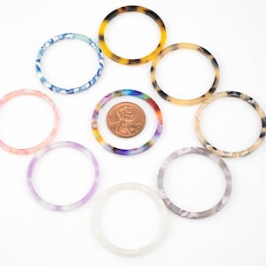 May include: Assortment of colorful and patterned plastic hair scrunchies in various colors, including blue, pink, purple, and brown. A penny is included for size reference.