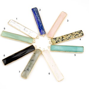 Puede incluir: Nueve colgantes de barra de piedras preciosas diferentes con detalles dorados. Los colgantes están dispuestos en círculo, con los números del 1 al 9 escritos junto a cada colgante.