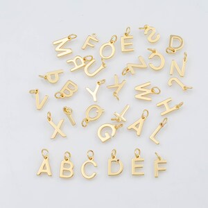 May include: A collection of gold-colored alphabet charms, each with a small loop for attaching to a chain or bracelet. The letters are in a variety of fonts and sizes, perfect for personalized jewelry. The letters A, B, C, D, E, and F are in a block font.