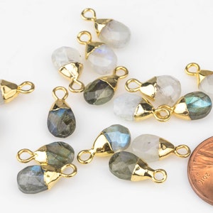 May include: A collection of gold-plated gemstone pendants in a teardrop shape. The gemstones are a mix of white moonstone and labradorite. The pendants have a jump ring for attaching to jewellery.