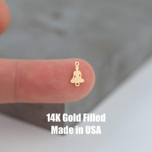 May include: A gold-filled charm featuring a small, detailed silhouette of a person sitting in a meditative pose. The charm has a jump ring for attaching to jewelry. 14K Gold Filled Made in USA.