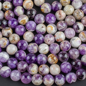 May include: A strand of round, purple amethyst beads with white and brown inclusions. The beads are smooth and polished.