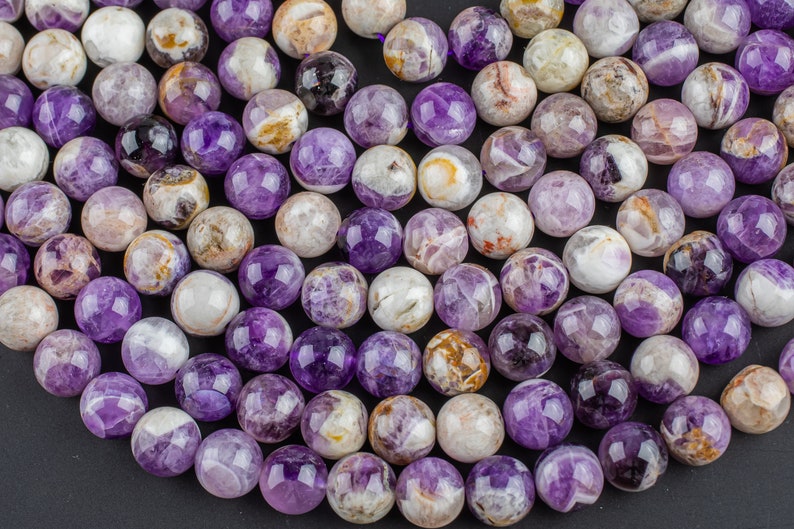 May include: A strand of round, purple amethyst beads with white and brown inclusions. The beads are smooth and polished.