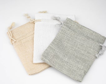 May include: Three small drawstring bags made of natural fabric. The bags are beige, white, and gray.