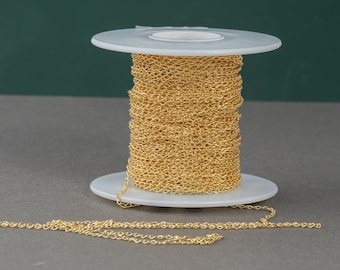 Könnte beinhalten: Eine Spule mit goldener Kette, die um eine weiße Kunststoffspule gewickelt ist. Die Kette ist in einem zarten, feinmaschigen Stil.