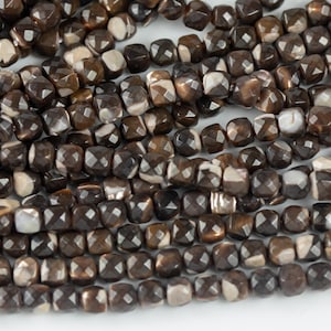 May include: A strand of brown and white gemstone beads with a faceted, square shape.
