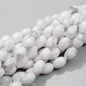 May include: A strand of white howlite beads, each bead is oval shaped and has a smooth, polished finish. The beads are strung together to create a necklace or bracelet.