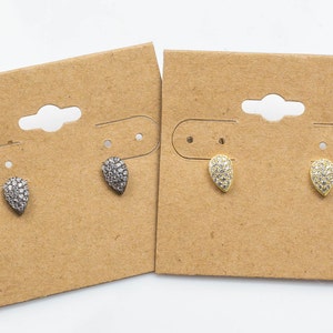 May include: Two pairs of teardrop-shaped earrings with a pave setting of clear stones. One pair is silver and the other is gold. The earrings are displayed on brown cardboard earring cards.