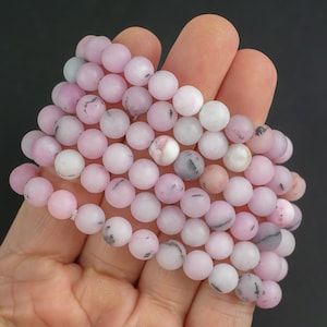 Puede incluir: Una hebra de cuentas de piedras preciosas rosadas y blancas. Las cuentas son redondas y tienen un acabado mate.