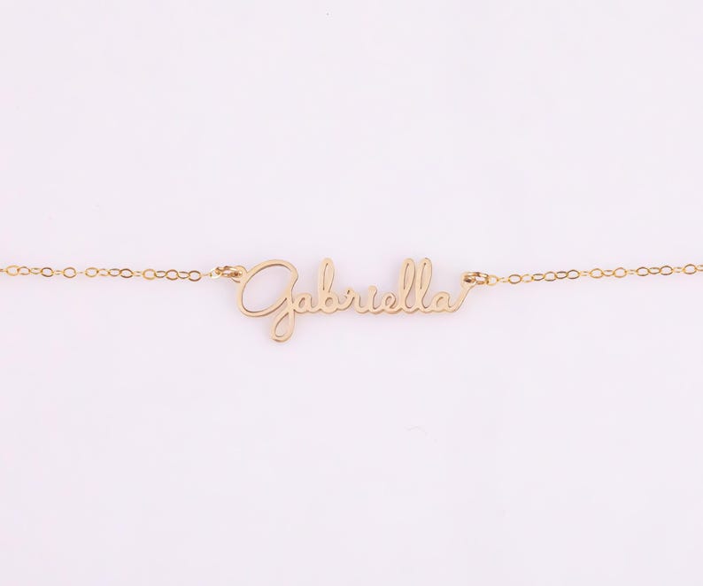 May include: A gold necklace with the name "Gabriella" written in cursive script.