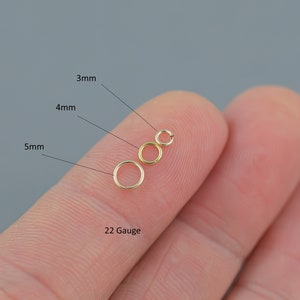 May include: Three gold-colored jump rings in 3mm, 4mm, and 5mm sizes, with a 22-gauge thickness. The rings are displayed on a fingertip against a gray background. The sizes are labeled with black text.