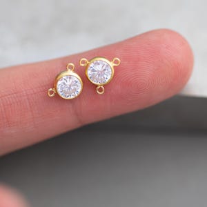 以下が含まれることがあります： クリアなキュービックジルコニアストーンが付いた、ゴールドトーンの丸いコネクターチャーム2個。各チャームには、ジュエリーを取り付けるためのループが3つあります。