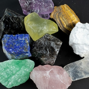 May include: A collection of ten rough, natural gemstones in various colors, including amethyst, yellow calcite, tiger's eye, white howlite, clear quartz, green aventurine, black obsidian, rose quartz, and lapis lazuli.