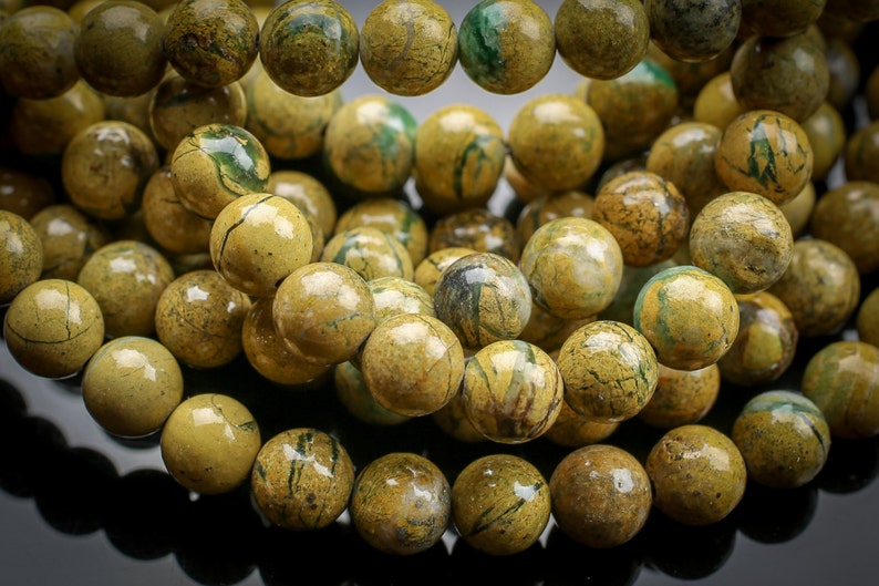 Peut inclure: Un collier de perles de jaspe jaune et vert. Les perles sont rondes et ont une finition lisse et polie. Le jaspe pr&eacute;sente un motif unique de couleurs et de veines tourbillonnantes.