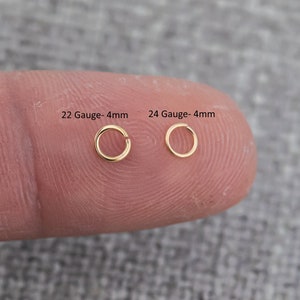 May include: Two gold nose rings, one 22 gauge and one 24 gauge, both 4mm in diameter. The rings are shown on a finger.