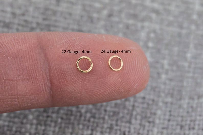 May include: Two gold nose rings, one 22 gauge and one 24 gauge, both 4mm in diameter. The rings are shown on a finger.