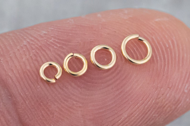 May include: Four gold jump rings of different sizes, arranged in a row from largest to smallest.