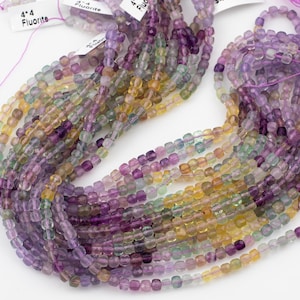 May include: A strand of multi-colored fluorite beads. The beads are a mix of purple, yellow, and green. The beads are faceted and have a square shape. The beads are strung on a white string. The beads are 4mm in size. The beads are labeled "4-4 Fluorite".