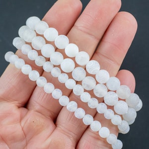 May include: Four strands of white agate beads, each strand with round, smooth beads. The beads have a frosted, matte finish.